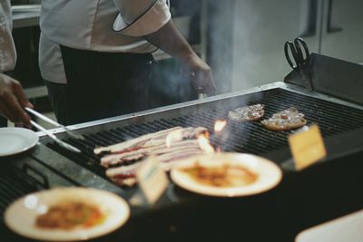 Midsection of chefs grilling beef meat on barbecue grill