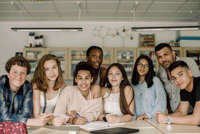 Portrait of professor with teenage students by table in classroom