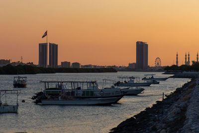 Boats in sea by buildings against sky during sunset