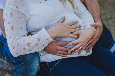 Midsection of pregnant couple touching abdomen