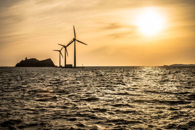 Silhouette of traditional windmill by sea against sky during sunset