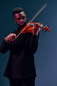 Midsection of man playing violin against blue background