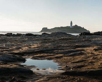 Lighthouse on beach by sea against sky