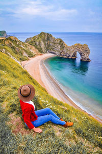 A woman wearing a hat is sitting and watching the beautiful scenery at durdle door, dorset, england.