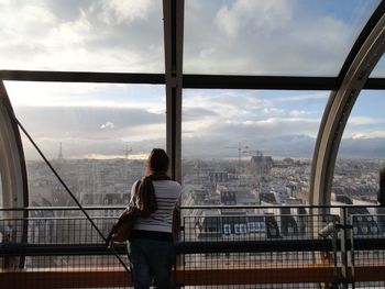 Rear view of woman standing by railing in city against sky