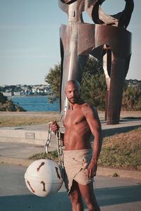 Full length of shirtless man holding ball in sea against sky