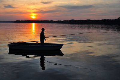 Silhouette of fisher in boat, lake at sunset