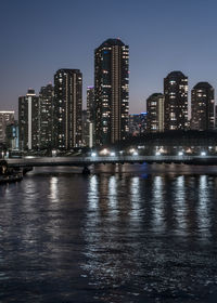 River by illuminated buildings in city against sky at night