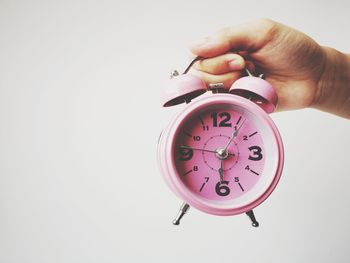 Close-up of hand holding clock against white background