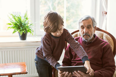 Boy assisting great grandfather in using digital tablet at home