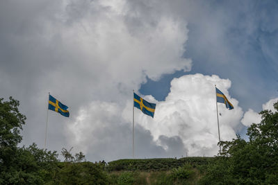 Low angle view of swedish flags against cloudy sky