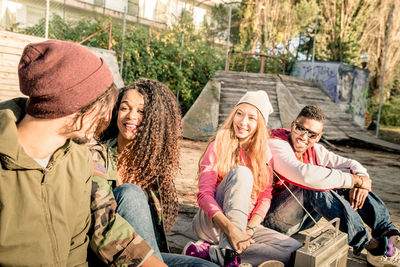 Happy friends talking while sitting against trees