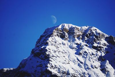 Low angle view of snowcapped mountains against clear blue sky