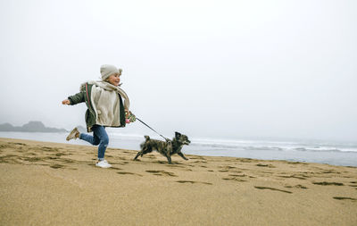 Happy girl running with dog on the beach on a foggy winter day