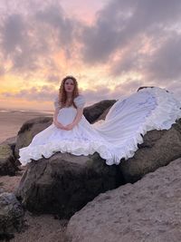 Woman sitting on rock against sky during sunset