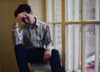 Tired man with head in hands while sitting by window at home