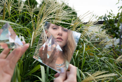 Reflection of woman holding prism in mirror against plants