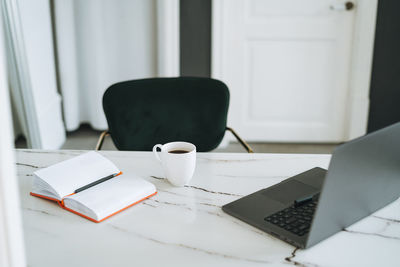 Working place with cup of coffee, notes and open laptop on white marble table in office room