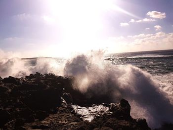 Waves splashing on rocks at shore against sky