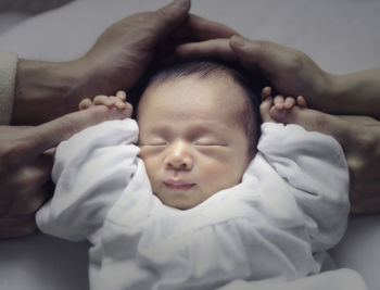 Cropped hands of people by baby lying on bed at home