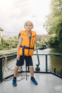 Full length of confident boy steering boat in river against sky