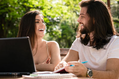 Smiling friends using laptop while sitting at table