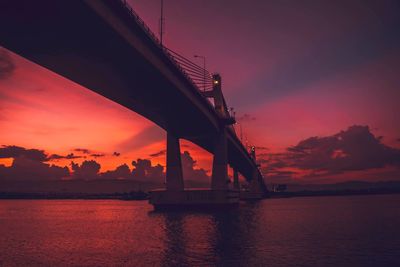 Silhouette bridge over sea against orange sky