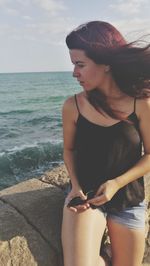 Young woman sitting on retaining wall by sea