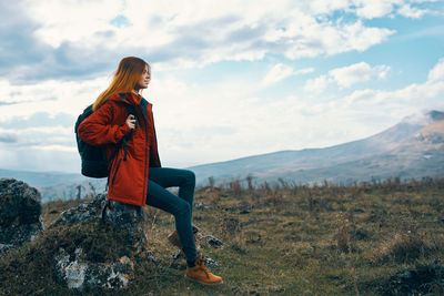 Woman sitting on mountain against sky