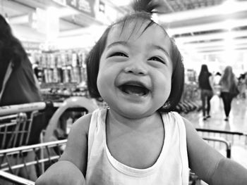Close-up of happy cute baby girl sitting in shopping cart at supermarket