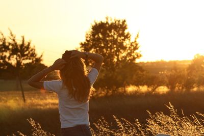 Rear view of woman standing on field during sunset