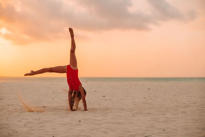 Full length of man with arms raised on beach against sky during sunset