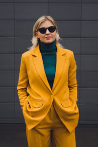 Portrait of young woman standing against yellow background