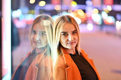 Portrait of smiling young woman in illuminated city at night