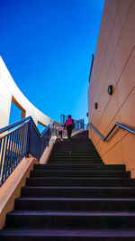 Low angle view of siblings walking on stairs against clear blue sky