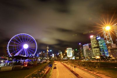 Illuminated ferris wheel in city against sky at night