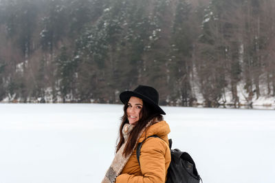 Portrait of a happy young woman standing by frozen lake. ice, snow, cold weather, hat.
