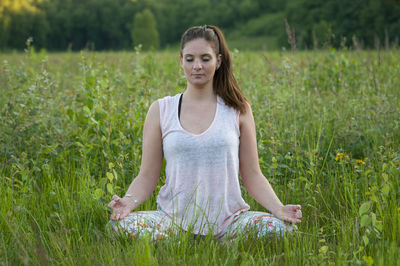 Beautiful young woman meditating while sitting on grassy field