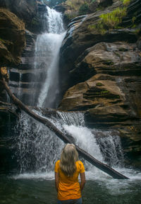Rear view of man surfing in waterfall