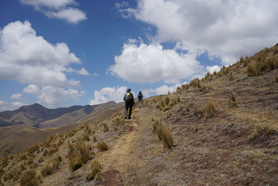 Rear view of hikers hiking on mountain against cloudy sky