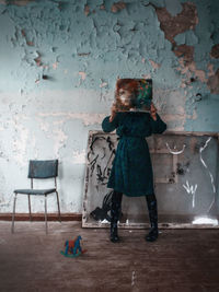 Full length of woman holding artwork while standing in abandoned room