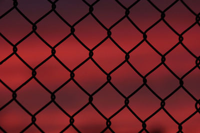 Full frame shot of silhouette chainlink fence against red sky during sunset