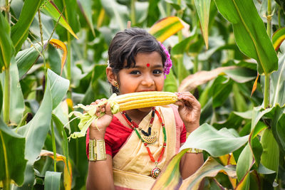 Portrait of cute girl eating corn while standing amidst plants