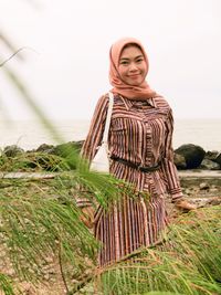 Portrait of smiling young woman standing on land against sky