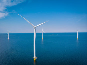 Wind turbines in sea against blue sky, windmills by sea against sky, windmills park westermeerdijk