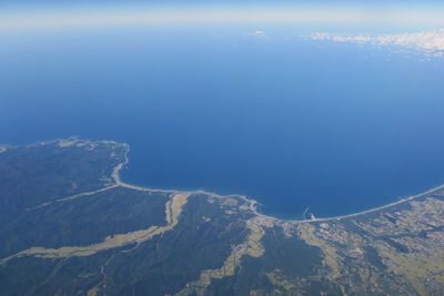 Aerial view of sea and mountains against blue sky