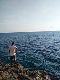 Rear view of man standing on rock by sea against sky