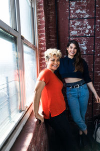 Portrait of happy female friends standing by window at home