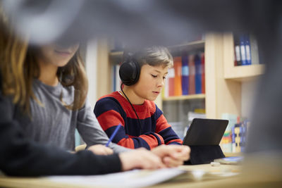 Boy wearing headphones while looking at digital tablet in classroom