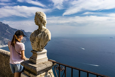 Statue and woman looking at sea against sky